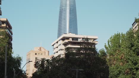 Tilt-up-of-car-driving-in-modern-Sanhattan-area-with-Gran-Torre-Santiago-skyscraper-in-background,-Chile