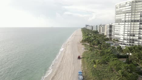 Aerial-follows-sandboni-as-it-cleans,-rakes-beach-sand-on-Miami-Beach