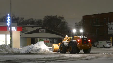 CAT-938M-Wheel-Loader-Shovelling-Snow-Beside-Road-In-Toronto-At-Night