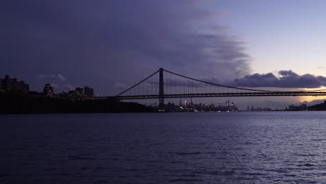 Boat-crossing-the-east-river-with-Brooklyn-suspension-bridge-and-skyline-of-New-York-City-at-distance-during-epic-sunset