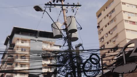 Close-up-tilt-shot-revealing-a-cabling-mess-on-an-urban-street-pole,-multiple-cables-and-connections-provide-power-and-communication-to-the-local-residents-and-businesses,-Panama-City