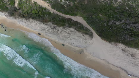 Spinning-aerial-tracks-vehicles-on-sandy-ocean-beach-in-Australia