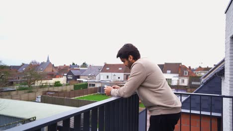 Young-handsome-man-standing-on-his-balcony-and-texting-on-his-phone
