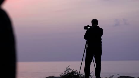 Silhouette-Eines-Männlichen-Fotografen,-Der-Während-Der-Blauen-Stunde-Eine-Fotokamera-Auf-Einem-Stativ-Am-Strand-Macht