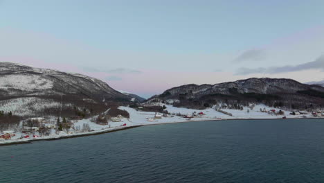 Beleuchteter-Himmel-Der-Polarnacht-In-Norwegen,-Häuser-An-Der-Küste-Mit-Schnee-Bedeckt