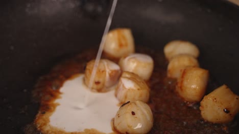 Seafood-dish-preparation,-chef-adding-three-spoons-of-coconut-milk-into-a-shallow-frying-pan-with-buttery-golden-brown-pan-grilled-scallops,-close-up-shot