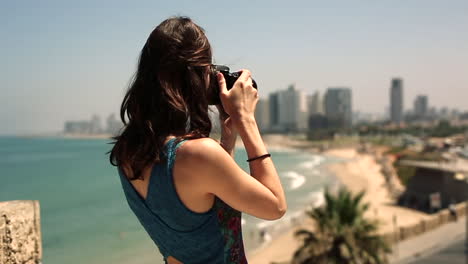 Back-view-of-woman-photographing-beach-and-city-skyline,-brunette-unrecognizable-tourist-photographer-woman-taking-photos