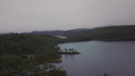 Drone-shot-flying-over-a-lake-and-forest-in-Norway-covered-in-fog-and-mist