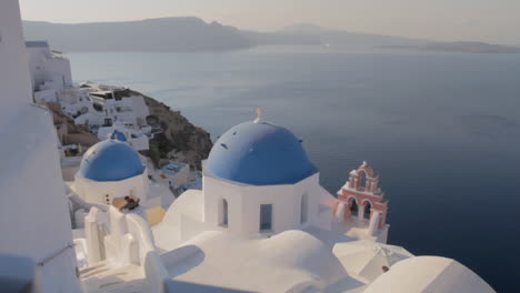 Blue-church-domes-and-pink-church-bell-overlooking-a-majestic-seascape-in-Oia,-Santorini