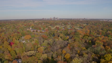 Flyover-of-autumn-trees-with-a-small-church-and-a-city-skyline-on-the-horizon