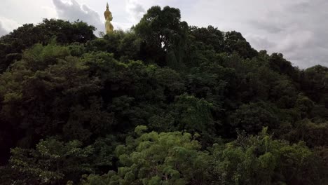 A-slow-aerial-shot-revealing-a-statue-of-Buddha,-temple-and-fields-in-the-distance