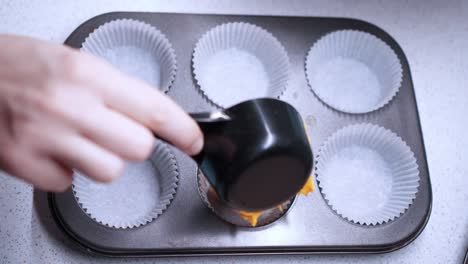 Female-hand-pours-yellow-cupcake-batter-into-a-six-baking-cup-oven-tray