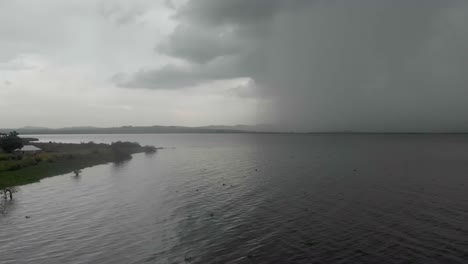 Aerial-shot-flying-low-over-Lake-Victoria-with-a-big-storm-pouring-down-rain-on-the-horizon