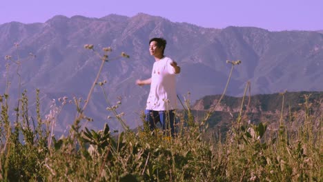 Asian-male-street-dancer-dancing-Locking-and-grooving-in-the-mountains-with-purple-sky-and-grassy-foreground