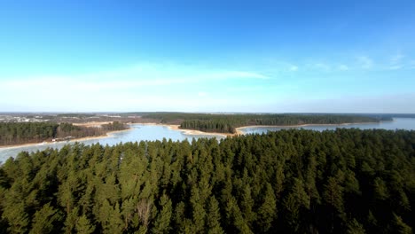 Aerial-closing-in-shot-of-an-enormous-frozen-lake-and-spruce-forest-during-winter-season,-Poland