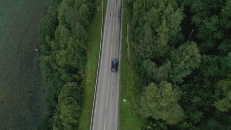 Aerial-Slomo-Top-shot-of-Blue-Nissan-driving-Solo-on-a-Norwegian-road,-surrounded-by-Trees
