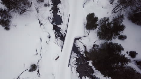 Aerial-view-of-a-small-bridge-over-a-creek-in-a-snowy-valley-in-the-alps,-Kleinwalsertal,Austria
