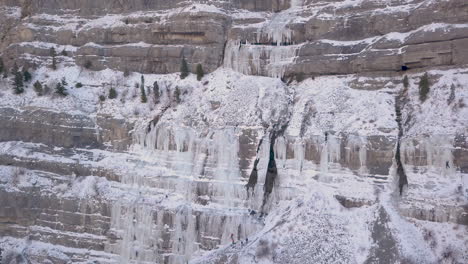 Ein-Gefrorener-Wasserfall-Entlang-Einer-Schroffen-Klippe-Mit-Bergsteigern-Am-Fuße-Des-Eises,-Die-Hinaufklettern-Und-Herauszoomen
