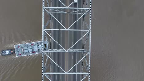 AERIAL:-Overhead-birds-eye-view-of-bridge-and-traffic,-with-a-construction-boat-passing-underneath