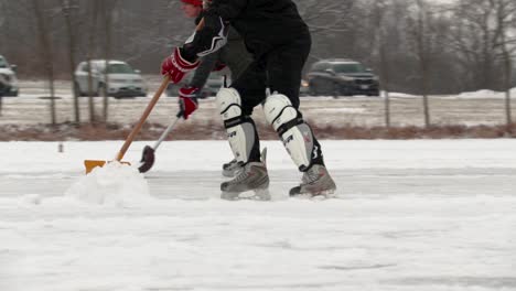 Slow-motion-tracking-shot-of-an-adult-skating-and-removing-snow-from-pond-hockey-field