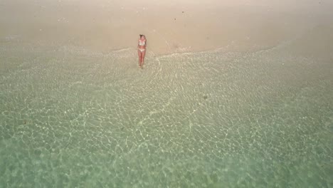 Aerial-view-of-young-caucasian-woman-in-bikini-on-white-sandy-beach-in-Asia---camera-tracking-backwards