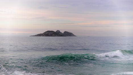 Wunderschöne-Insel-Am-Horizont-Direkt-Vor-Der-Küste-Von-Rio-De-Janeiro-Mit-Hereinbrechenden-Wellen-Im-Vordergrund-Und-Dem-Farbenfrohen-Sonnenaufgangshimmel-Im-Hintergrund