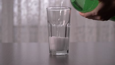 Pouring-transparent-sparkling-soda-into-tall-glass-in-slow-motion,-straight-ahead-shot