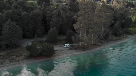 Motorhome-on-beach-beautiful-blue-Lake-Wakatipu,-Queenstown,-New-Zealand-and-trees-scenery-during-fall-autumn---Aerial-Drone