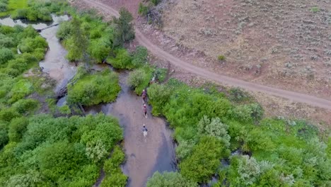 Drone-footage-of-cowboys-on-horseback-riding-upstream-in-the-rocky-mountains