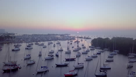 Aerial-high-angle-fly-over-boat-filled-harbor-away-from-pink-sunrise