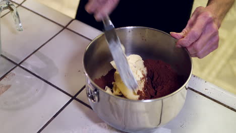A-chef-in-a-kitchen-putting-vegan-butter-into-a-metal-mixing-bowl-while-baking-a-chocolate-cake-for-dessert