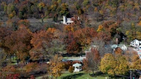 Aerial-dolly-move-past-the-Berkeley-Springs-State-Park-showing-the-castle-on-the-hill-above,-Roman-Baths,-gazebo-and-autumn-colors