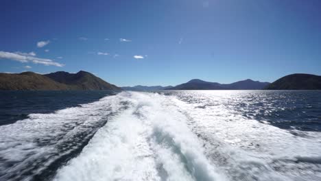 Back-of-the-boat-waves-with-blue-sky-and-mountains-in-background