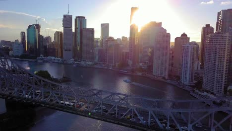 Forward-aerial-view-of-a-city-with-tall-buildings-and-a-car-bridge-over-a-river-at-sunset