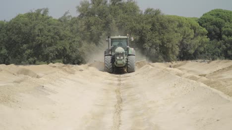 Green-tractor-with-motor-grader-plowing-rows-on-farm-in-Huelva,-Spain,-SLOWMO