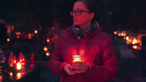 Woman-visiting-graveyard-at-night-holding-burning-candle