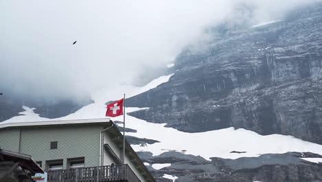 Swiss-Flag-waving-dramatically-with-birds-flying-in-slow-motion-at-Eigergletscher-mountains