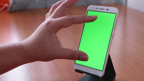 Slide-motion-of-the-male-hand-is-sliding-and-touching-the-phone-with-the-green-screen-is-placed-on-the-pedestal-on-the-wooden-table