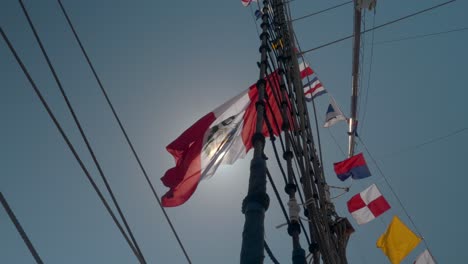 Flag-waves-in-breeze-high-above-on-colorful-tallship-mast-and-rigging