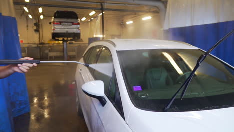 Worker-spraying-water-and-washing-the-windows,-of-a-white,-Suv-car,-at-a-Carwash,-in-Sweden