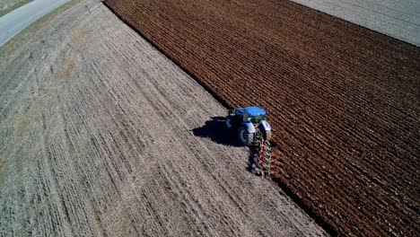 Luftaufnahme-Mit-Fokus-Auf-Einen-Blauen-Traktor,-Der-Ein-Feld-Pflügt-Und-Dabei-Die-Farbe-Des-Bodens-Verändert