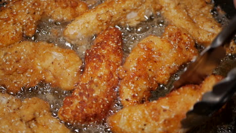 Crumbed-breast-chicken-tenderloins-turned-in-peanut-oil-in-a-pan-with-tongs