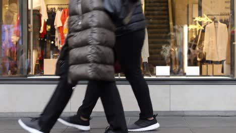 Close-up-on-feet-as-shoppers-walk-past-a-high-end-store