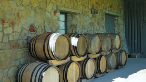 Stacked-wine-barrels-against-rough-rock-wall-on-farm