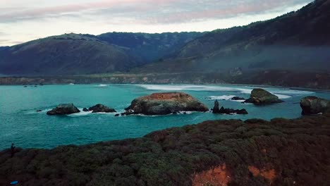 Twilight-aerial-wide-view-of-huge-ocean-cliffs-and-waves-crashing-on-rocks-at-Sand-Dollar-Beach-in-Big-Sur-California