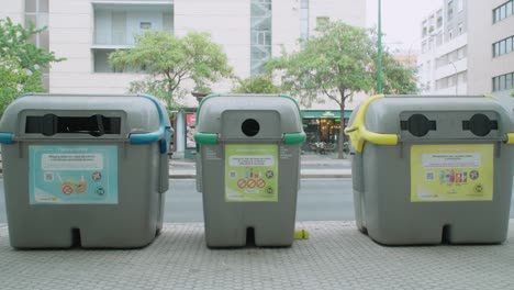 Recycling-bins-on-sidewalk-curb-in-Seville,-Spain,-ZOOM-IN