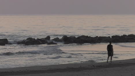 Man-walking-barefoot-on-seashore-at-dawn,-silhouette-slow-motion-seascape