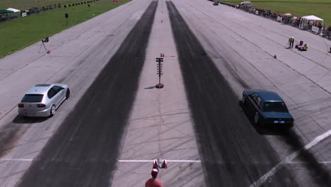 Aerial-follow-shot-of-two-cars-starting-a-drag-race-down-long-straightaway