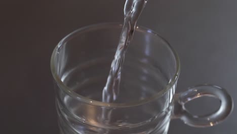 Above-angled-close-up-of-water-being-poured-into-a-glass-cup-on-a-metallic-kitchen-worktop,-health-and-clean-water-concept,-slow-motion-footage