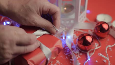 Tying-bow-on-Christmas-gift-with-ribbons-and-red-paper-with-red-background-and-baubles
